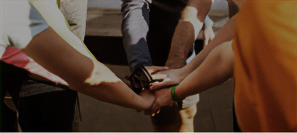 Group of 7 or 8 individuals in a circle, placing their hands on top of each other in a team exercise