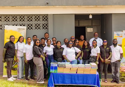 A team of 20 colleagues from Intertek Ghana stands behind a table of donated learning materials.