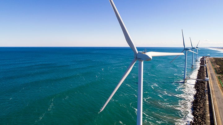 Beach-side wind turbines dotting a shoreline alongside a deserted road